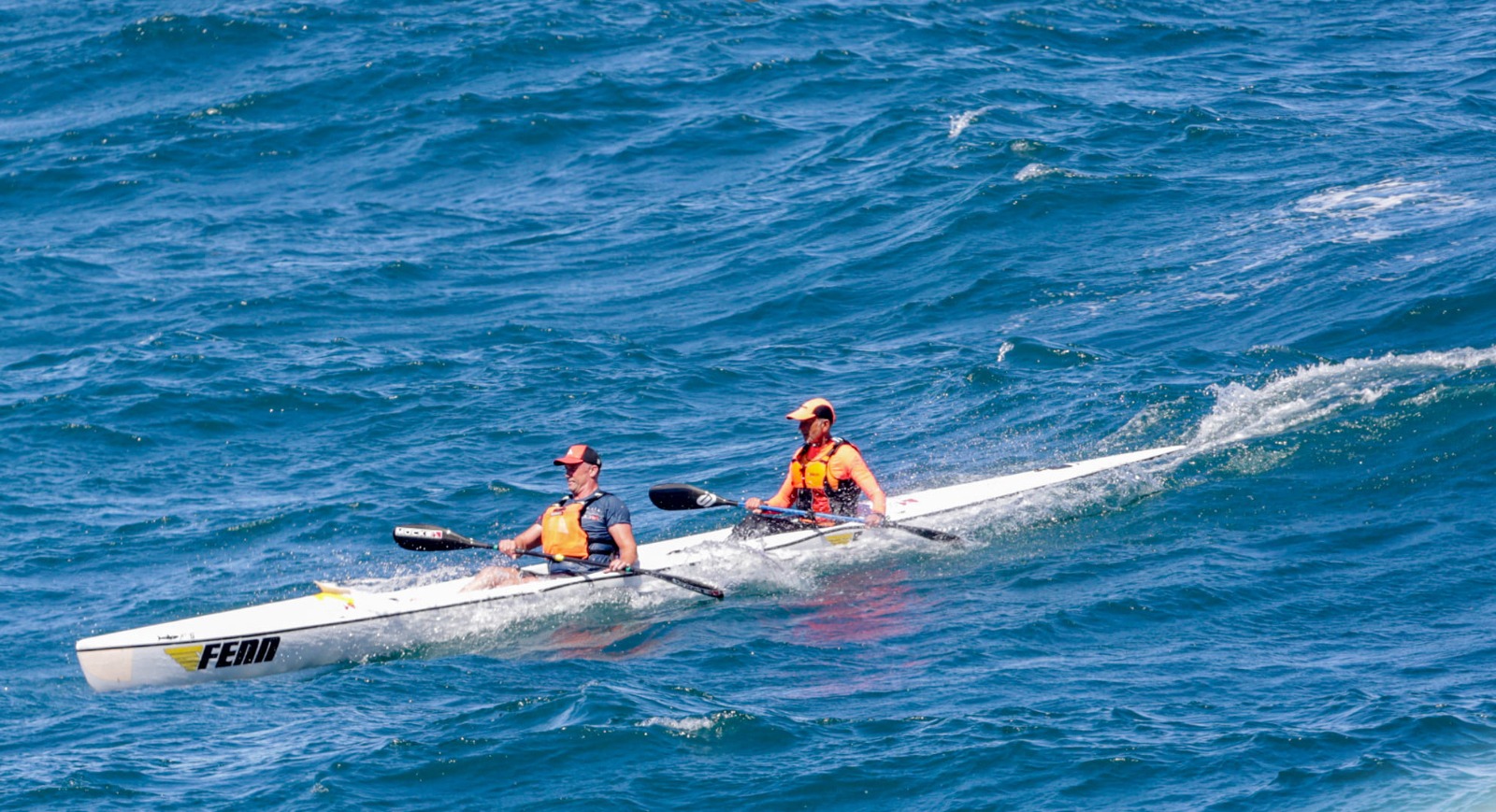 Two paddlers riding open-ocean swell in a tandem surfski