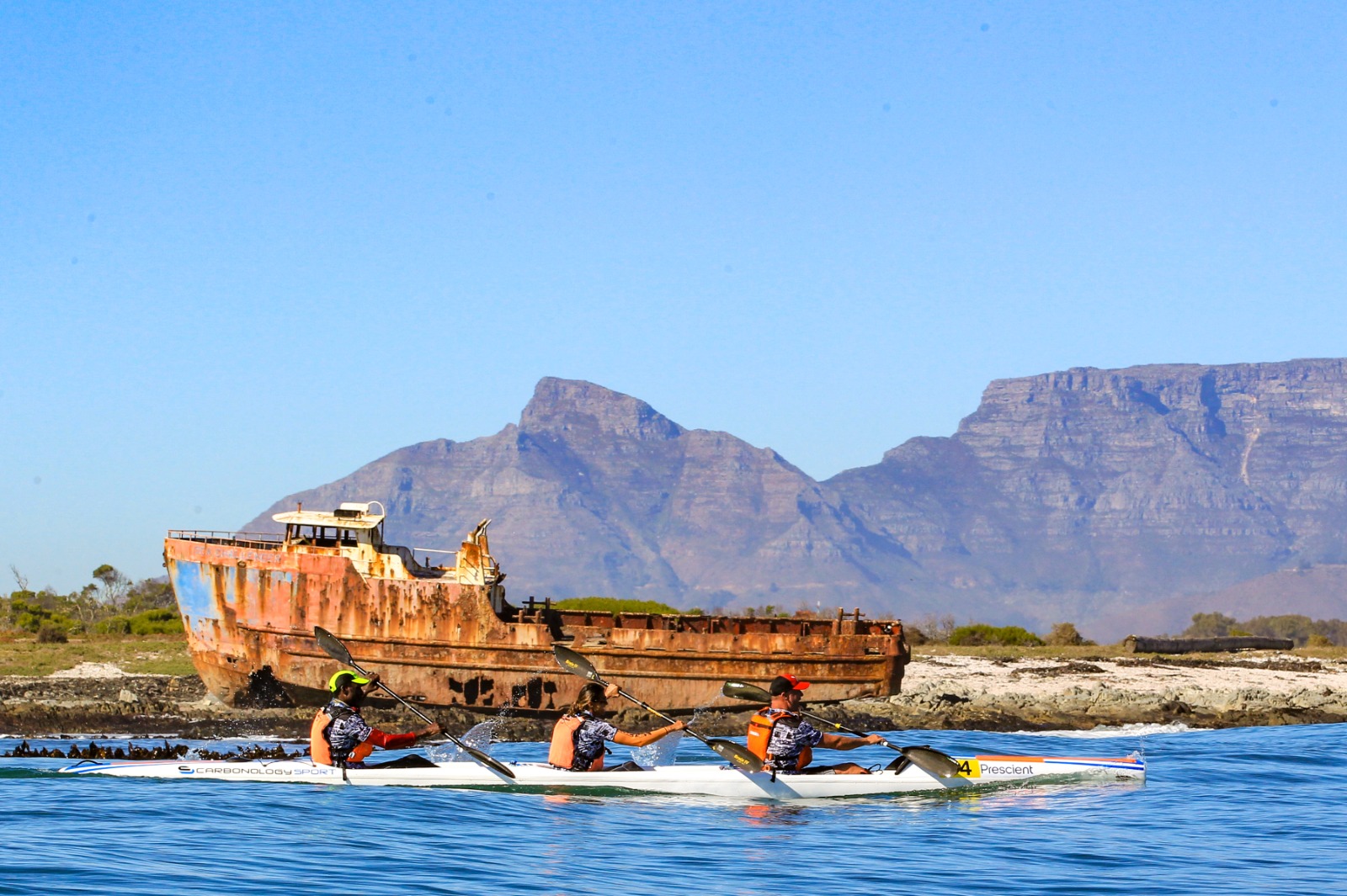 Surfski paddlers passing a coastal shipwreck with Table Mountain behind them