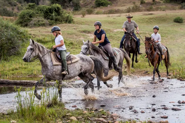 Riders crossing a shallow river on horseback at Botlierskop