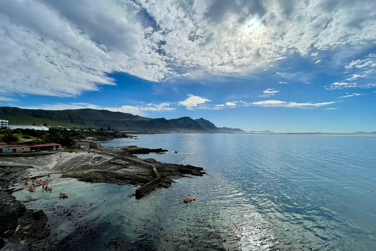Panoramic Hermanus cliffs and Walker Bay with kayakers below dramatic clouds